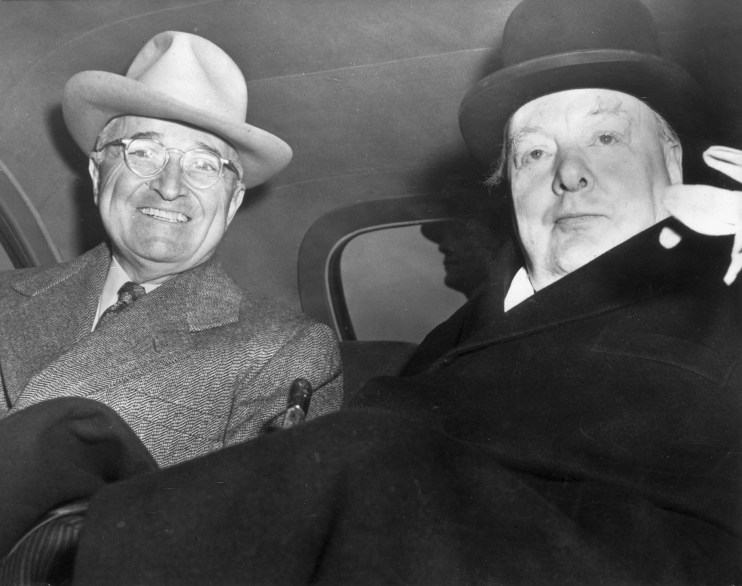 Harry Truman, smiling in a fedora, and Winston Churchill in a bowler hat, seated together in a car.