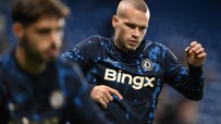 A male Chelsea FC player, possibly Mykhailo Mudryk, in a blue and black long-sleeved training top, stretching.