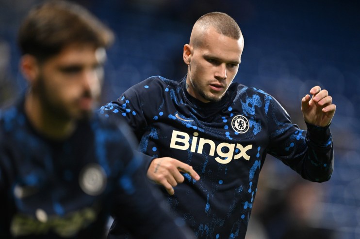 A male Chelsea FC player, possibly Mykhailo Mudryk, in a blue and black long-sleeved training top, stretching.