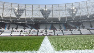 Football pitch with a white line, stadium seats, and bright lights under a clear sky.