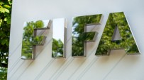 Reflective FIFA logo sign on a white wall, with green trees mirrored in the letters, under natural light.