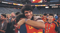 Carlos Alcaraz embracing a person, smiling, wearing a Rolex Daytona Rainbow watch at a stadium event