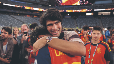Carlos Alcaraz embracing a person, smiling, wearing a Rolex Daytona Rainbow watch at a stadium event