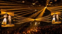ABBA Voyage concert with holograms of Agnetha and Frida performing, golden lights, and a live audience.