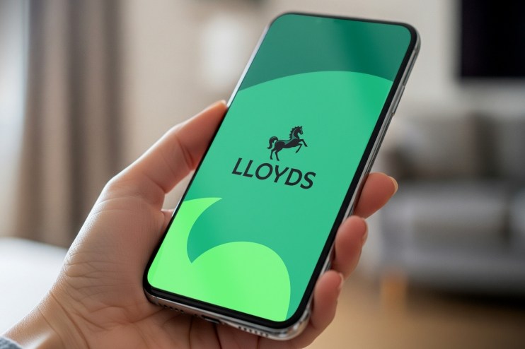 Hand holding a smartphone displaying the Lloyds Bank mobile app logo on a green screen.