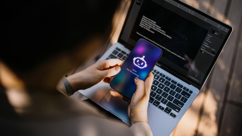A person interacting with a chatbot on a smartphone, with a laptop in the background, showcasing AI and technology.