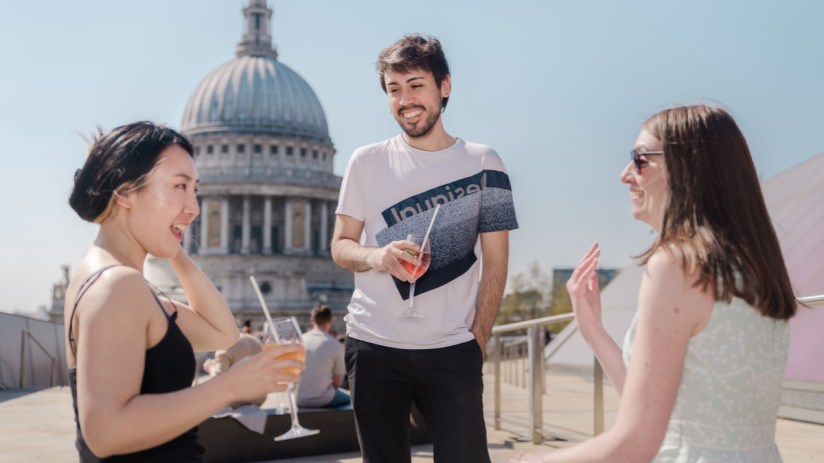 Three friends enjoying drinks on a rooftop bar with St Pauls Cathedral dome in the background.