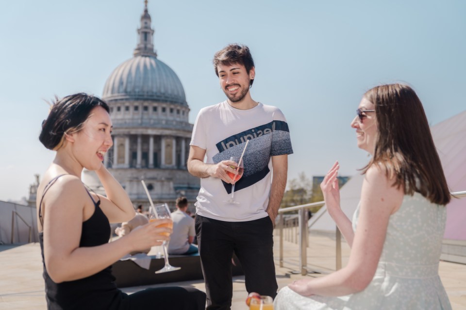 Friends enjoying drinks on a sunny London rooftop with St. Pauls Cathedral in the background.