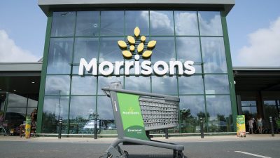 Green Instacart shopping cart outside a modern Morrisons supermarket entrance with large glass windows