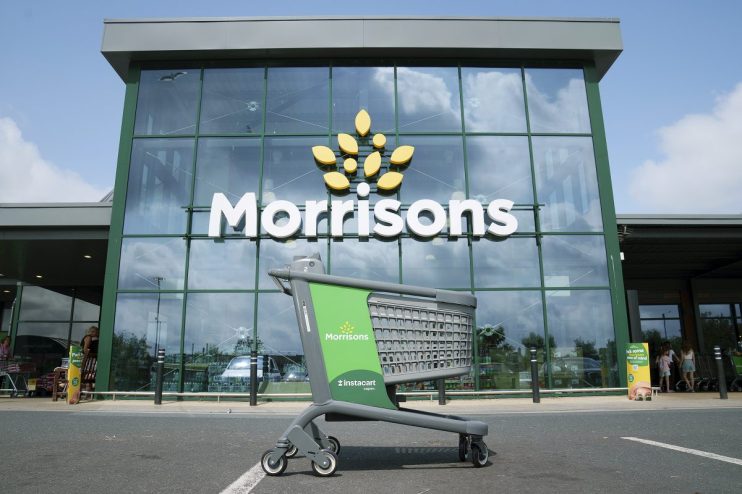 Green Instacart shopping cart outside a modern Morrisons supermarket entrance with large glass windows