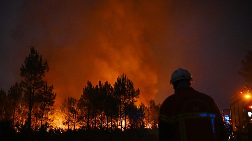 Firefighter in helmet and uniform watching a blazing forest fire at night, red glow in the sky