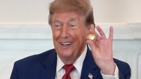 Donald Trump smiling and holding a small golden ball, wearing a blue suit and red tie.