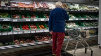 Shopper in a supermarket produce aisle browsing various packaged vegetables and fruits.