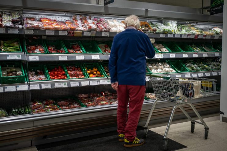Shopper in a supermarket produce aisle browsing various packaged vegetables and fruits.