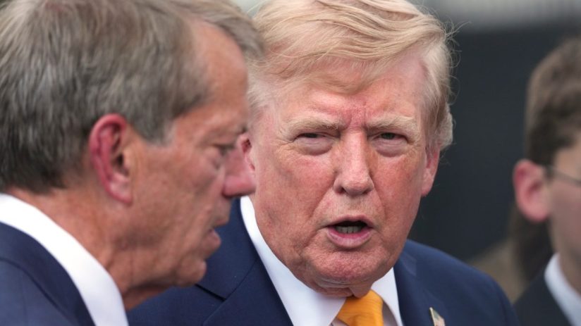 Donald Trump speaking with a man in a navy suit and blue tie outdoors