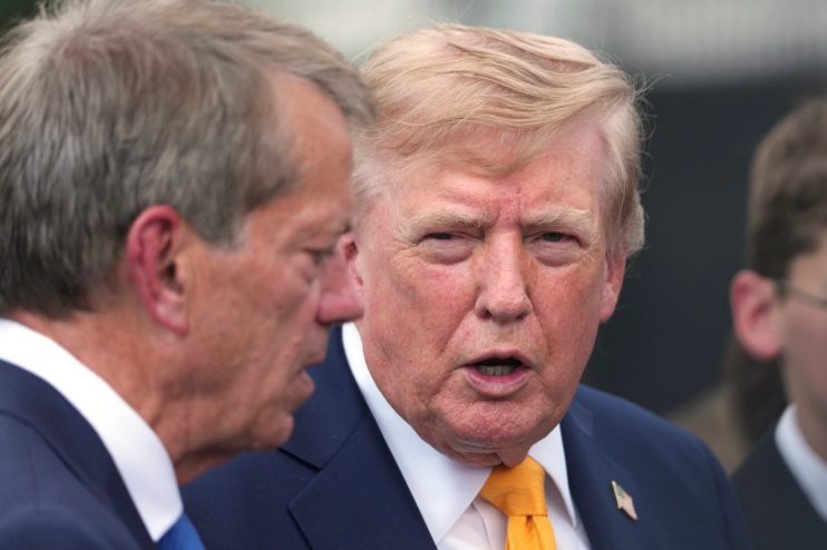 Donald Trump speaking with a man in a navy suit and blue tie outdoors
