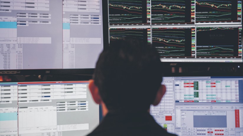 Trader monitoring multiple computer screens displaying stock market data, charts, and financial figures.