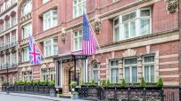 Exterior of The Stafford London hotel, a brick building with British and American flags, elegant windows, and ornate raili...