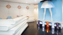 Modern reception area with unique legs art installation, white desk, and colorful stools.
