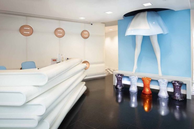 Modern reception area with unique legs art installation, white desk, and colorful stools.