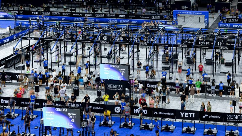 Elevated view of a CrossFit competition floor with multiple athletes, equipment, and large XENOM branding.