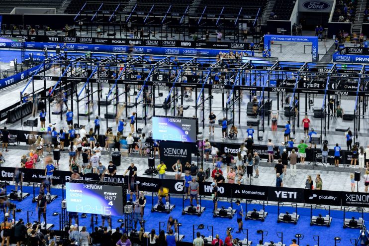 Elevated view of a CrossFit competition floor with multiple athletes, equipment, and large XENOM branding.