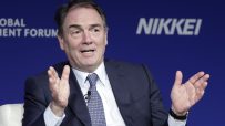 Alan Parker speaking at a business forum, gesturing with hands, blue background with NIKKEI and FORUM visible