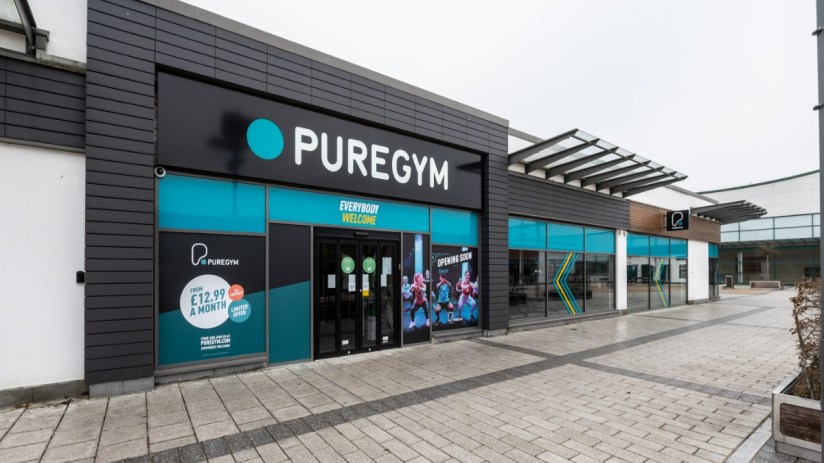 Exterior view of PureGym Aldershot, a modern fitness center with large windows and promotional signage