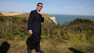 Andy Burnham adjusting his tie, overlooking white cliffs and the sea on a sunny day