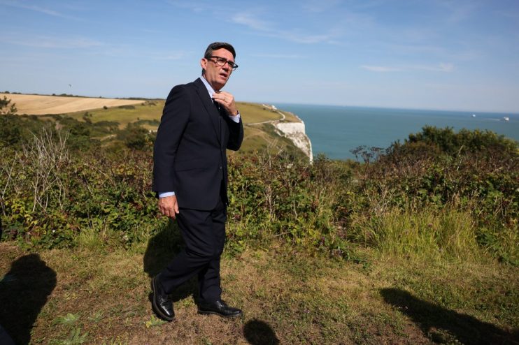 Andy Burnham adjusting his tie, overlooking white cliffs and the sea on a sunny day