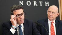 Andy Burnham and John Healey at Number 10 North, both wearing suits and ties, with a microphone in the foreground.
