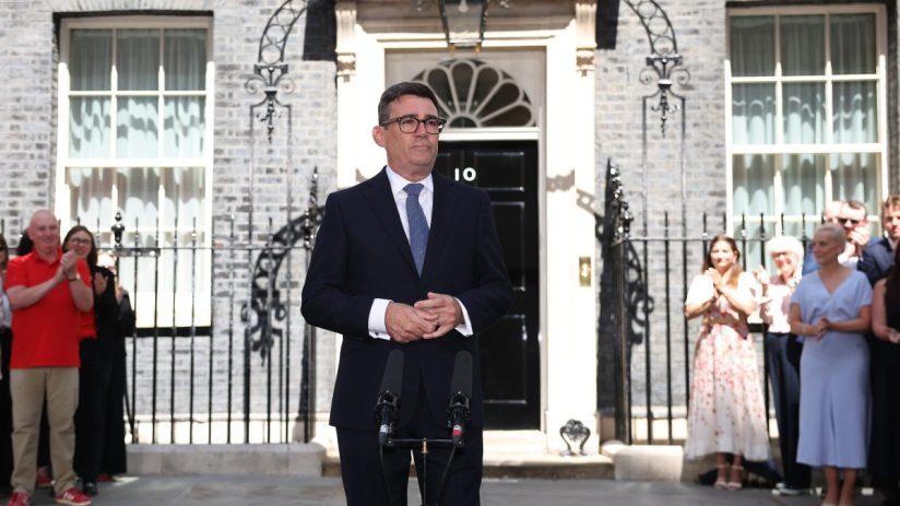 Andy Burnham, in a dark suit, speaks at a podium outside 10 Downing Street, with onlookers behind him