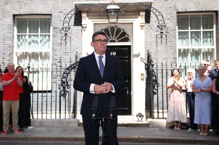 Andy Burnham, in a dark suit, speaks at a podium outside 10 Downing Street, with onlookers behind him