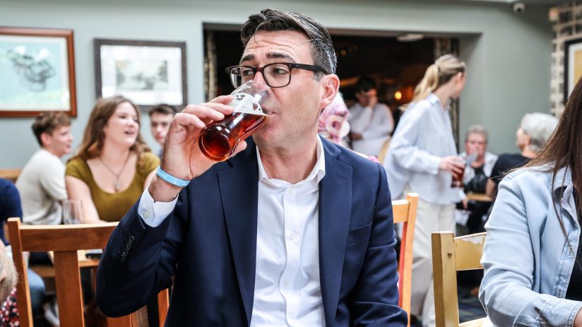 Andy Burnham, Mayor of Greater Manchester, drinking a pint of beer in a busy pub setting