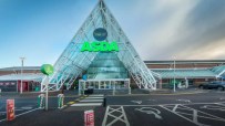 External view of a modern Asda supermarket entrance with a prominent green logo and glass pyramid-like structure.