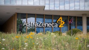 AstraZeneca building exterior with logo, glass facade, UK flag, and wildflowers in foreground.