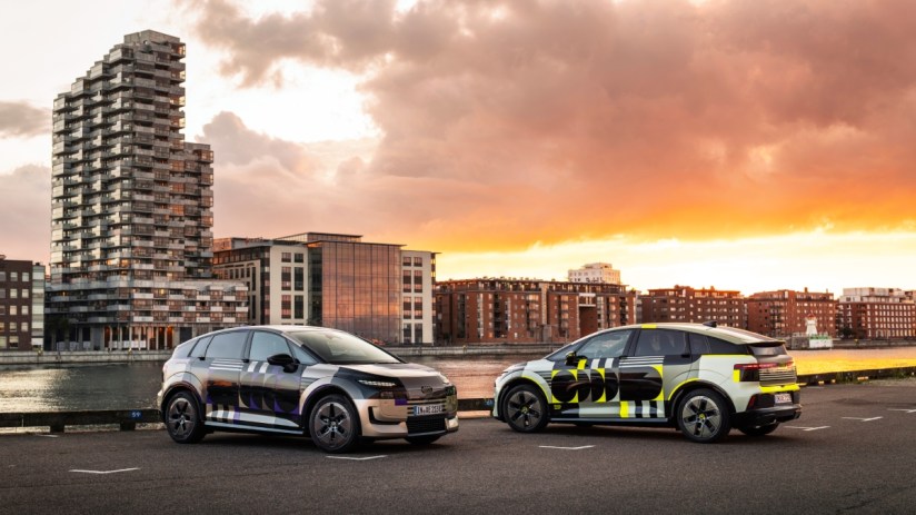Two Audi A2 concept cars with distinctive designs parked by a waterfront cityscape at sunset.