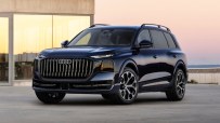 Dark blue Audi Q9 SUV parked on concrete with a modern building and sunset sky in the background.