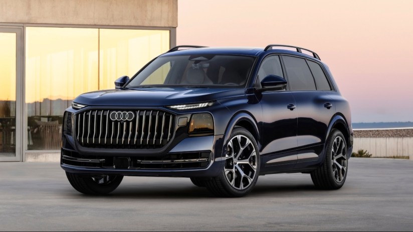 Dark blue Audi Q9 SUV parked on concrete with a modern building and sunset sky in the background.