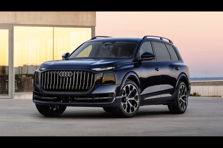 Dark blue Audi Q9 SUV parked on concrete with a modern building and sunset sky in the background.