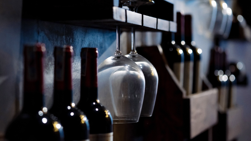 Wine bottles and hanging glasses on a dark wooden rack, suggesting a selection of Pinot Noir to buy.