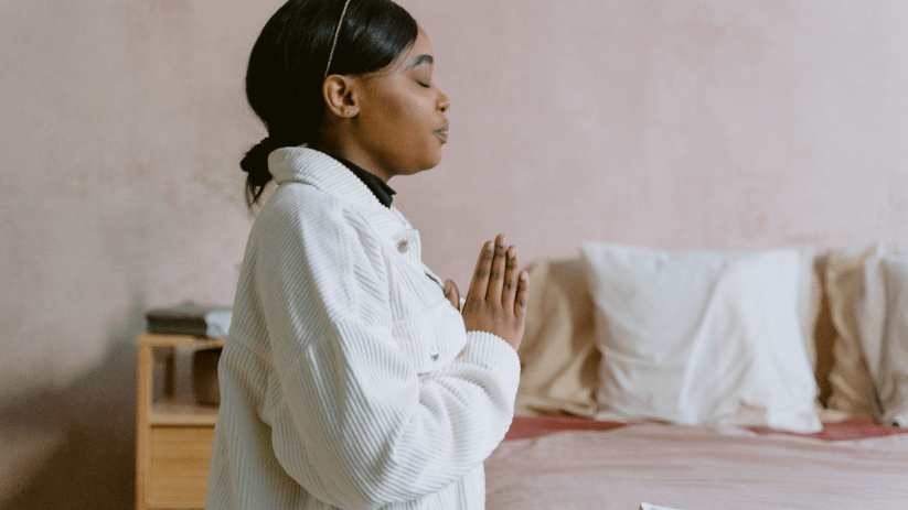Woman with closed eyes praying over an open Book of Common Prayer on a bed