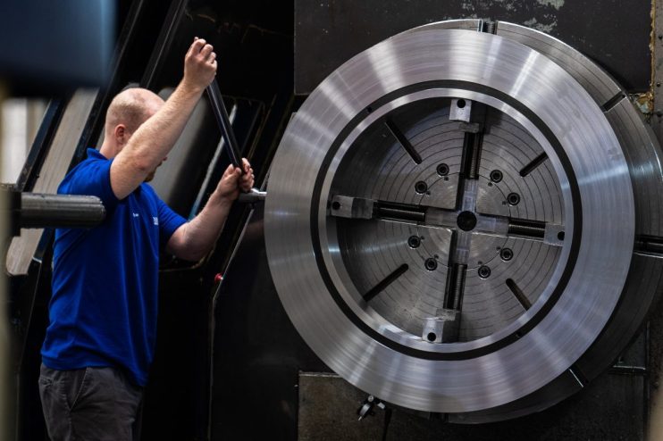 Technician in blue shirt operating a large metal lathe machine, industrial manufacturing process