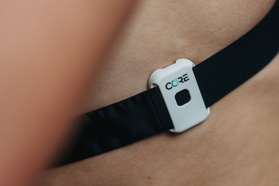 Close-up of a CORE body temperature monitor attached to a black strap on a persons skin.