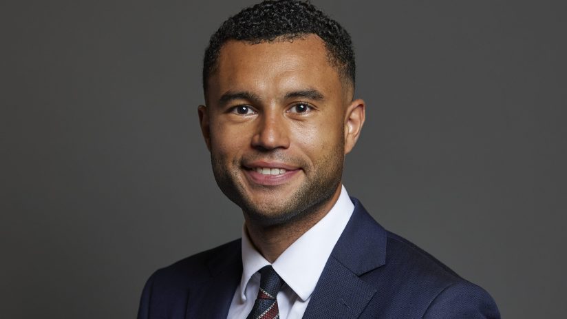 Callum Anderson, a smiling business professional in a navy suit and striped tie against a gray background.