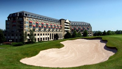 The Celtic Manor Resort in Newport, with a golf course bunker and green foreground under a clear sky.