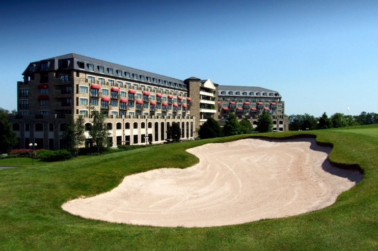 The Celtic Manor Resort in Newport, with a golf course bunker and green foreground under a clear sky.