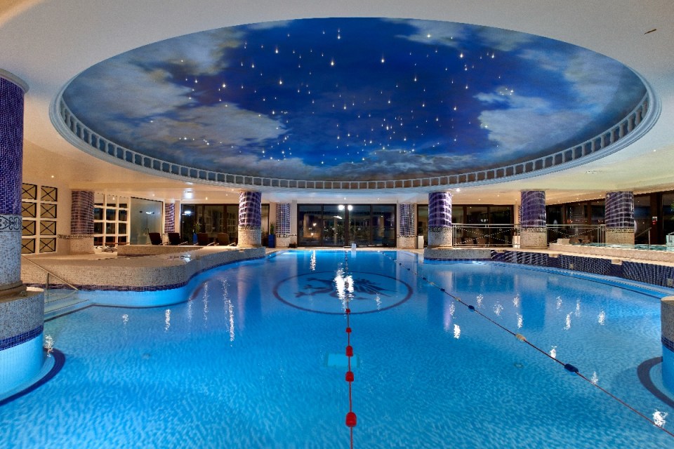 Indoor swimming pool at Celtic Manor with a starry sky ceiling, blue water, and mosaic-tiled pillars.