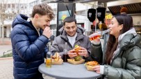 Three young adults enjoying chicken burgers and drinks from a food truck, casually dining outdoors.