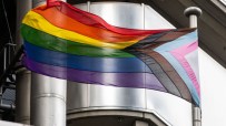 Progress Pride flag flying on a pole against a modern building, symbolizing trans policies in city firms